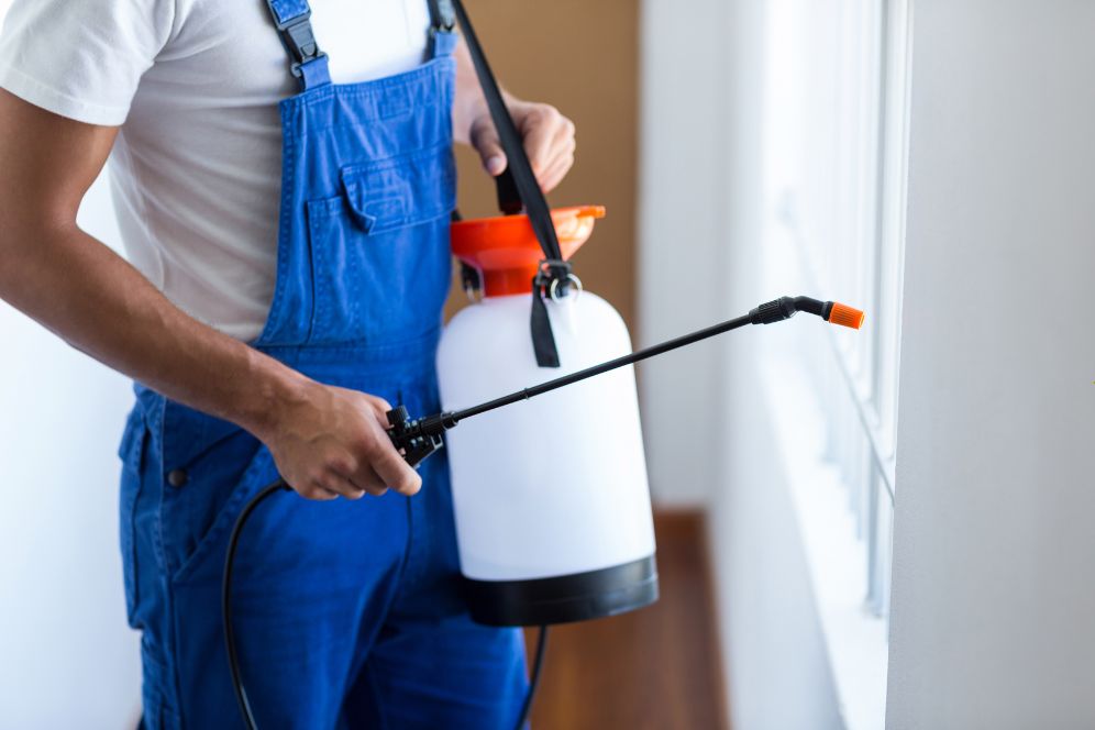 A man wearing overalls uses a sprayer on a window, illustrating a lawn pest control service in Chicago, IL.